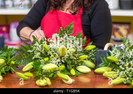 Woman florist wearing apron standing at counter making bouquet for client at flower shop . Stock Photo