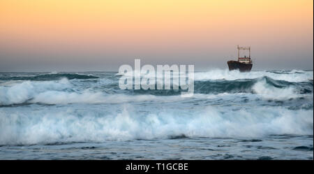 Abandoned ship in the stormy sea with big wind waves during sunset. Stock Photo