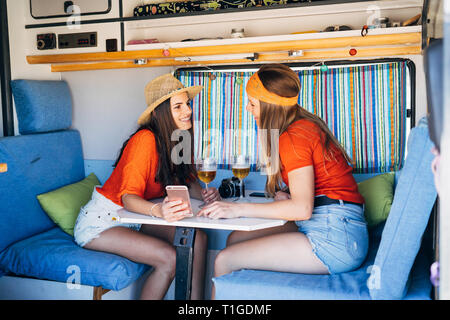 Two young women using smart mobile and toasting in their camper van Stock Photo