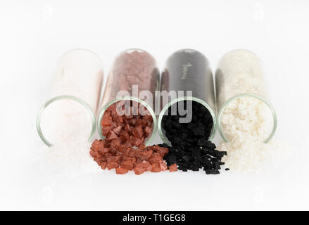 Alaea salt, hawaiian black salt, grey salt and fleur de sel pouring from jars and isolated now white. Stock Photo