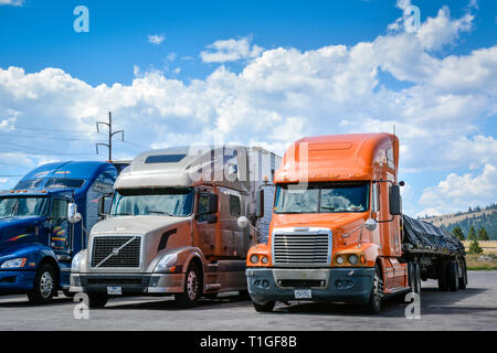 Three big rig trucks are parked at a truck stop in Montana on a cloudy day in the USA Stock Photo