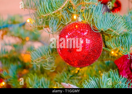 Glittering red bauble of a Christmas tree. Close up of the glittering red bauble of a Christmas tree. The vibrant Christmas ball is hanging on the bra Stock Photo