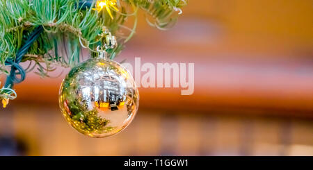 Reflective bauble hanging on a Christmas tree. Close up of the shiny bauble hanging on the branch of a Christmas tree. Reflection of the holiday tree  Stock Photo