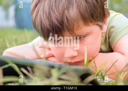 Child with ipad on green grass. Portrait of boy with tablet. Eye problems caused by using tablets too much. Health care concept. Boy with tablet in Stock Photo