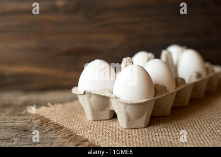 Raw white eggs in egg box on wooden background. Stock Photo