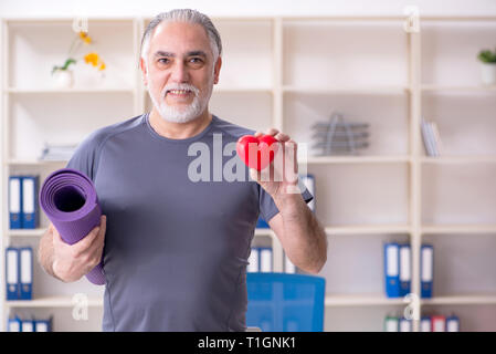 White bearded old man employee doing exercises in the office Stock Photo