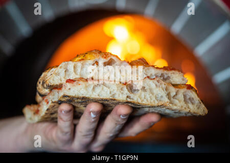 man/chef holding traditional roman Italian style wood fired pizza slices in front of a wood fired oven in a pizzeria/trattoria/restaurant. Stock Photo