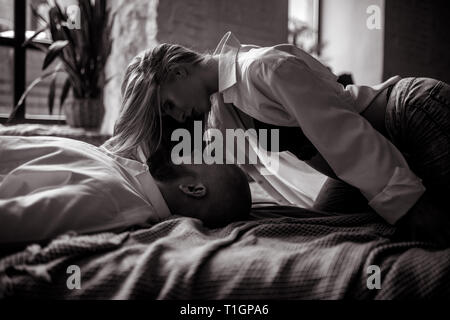 Pregnant woman lies with her husband on the bed. Black and white image. Stock Photo