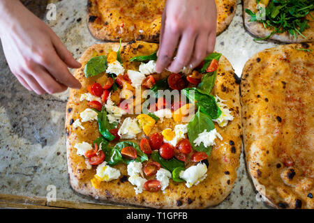 man's hands making preparing a colourful roman style italian pizza in a pizzeria/trattoria Stock Photo