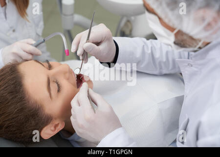 Woman with opened mouth lying on dentist chair with opned mouth. Professional doctor holding restoration instruments and treating teeth and mouth cavity for health care. Stock Photo
