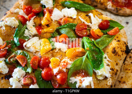colourful vegetarian Italian wood fired pizza with cherry tomatoes, basil and mozzerella in a trattoria/pizzeria Stock Photo