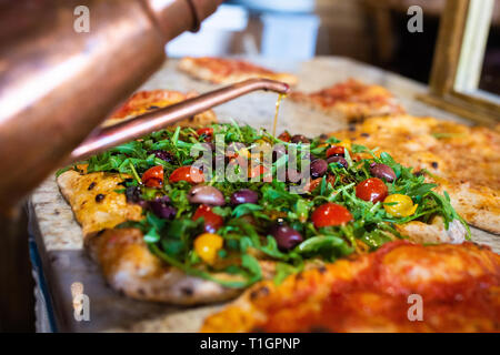 olive oil being drizzled onto an authentic roman style italian wood fired vegan pizza in a trattoria Stock Photo