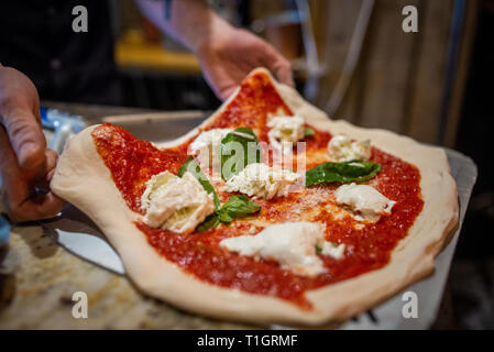 close up of a chef's hands preparing an authentic italian neapolitan margherita pizza in a pizzeria trattoria restaurant. Putting pizza on peel Stock Photo