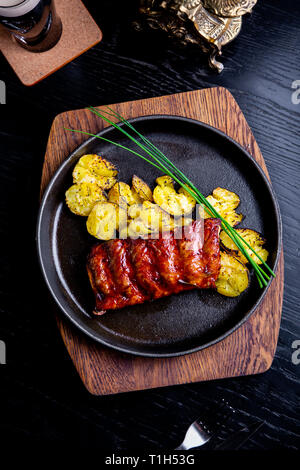 Close up Gourmet Main Dish with Grilled Pork Rib and Fried Potatoes on Black pan. Served on Wooden Board Stock Photo