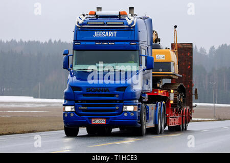 Jokioinen, Finland - March 23, 2019:  Blue Scania R580 conventional cab of Maansiirto Jeesarit Oy hauls tracked excavator on trailer along highway. Stock Photo