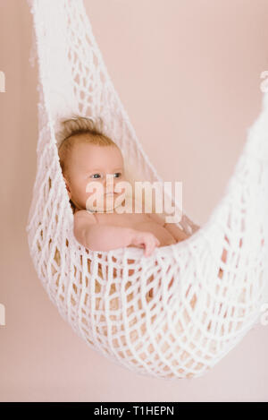Newborn Baby relaxing in a white hammock with soft bright background - happy family moments Stock Photo