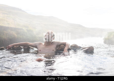 Young happy man swimming bathing relaxing in Hveragerdi Hot Springs in Reykjadalur during autumn morning day in south Iceland on golden circle rocks a Stock Photo
