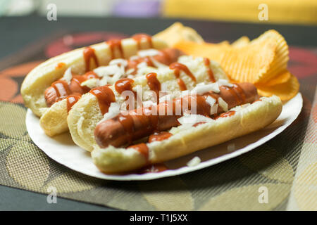 Two New York style hot dogs with ketchup, mustard, onions, and a side of potato chips, served on a paper plate Stock Photo