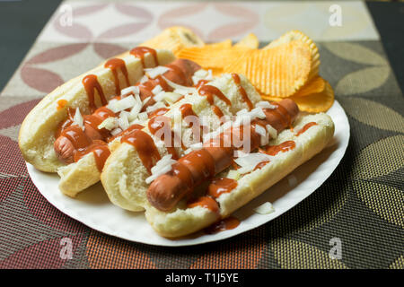 Two New York style hot dogs with ketchup, mustard, onions, and a side of potato chips, served on a paper plate Stock Photo