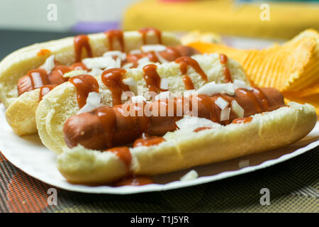 Two New York style hot dogs with ketchup, mustard, onions, and a side of potato chips, served on a paper plate Stock Photo