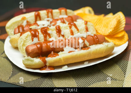 Two New York style hot dogs with ketchup, mustard, onions, and a side of potato chips, served on a paper plate Stock Photo