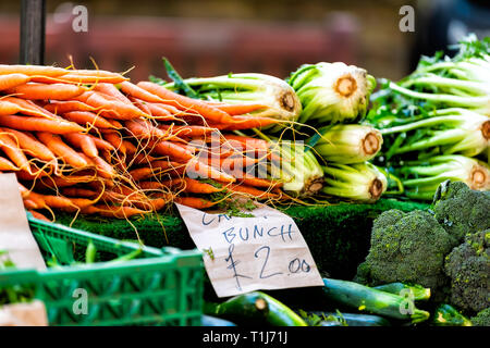 Closeup of many green and orange carrots with greens in farmer's market on display at stall bunches and price in English pounds in London Stock Photo
