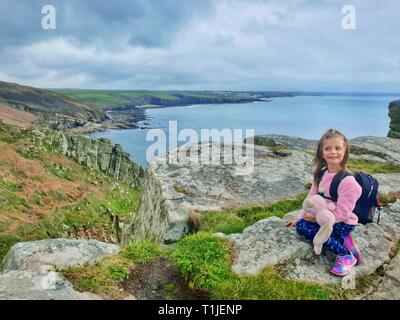 A small child resting on Trewavas Cliff, after a long hike from Porthleven in Cornwall, along the Southwest Coastal Path. Stock Photo