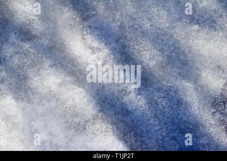 Macro abstract background of melting snow on a ground surface with tree shadows Stock Photo