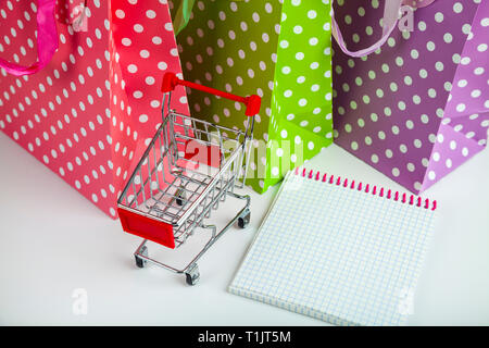 Three multi-colored shopping bags, notepad and shopping cart Stock Photo