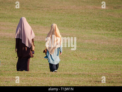Two Muslim women wearing traditional outfits walking over a field in the Johor State of Malaysia.