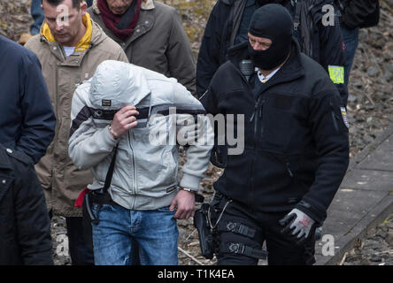 Wiesbaden, Germany. 27th Mar, 2019. Accompanied by two masked police officers, Ali B., accused of murdering 14-year-old Susanna, is led along a railway line near Erbenheim. Here the man, who came from Iraq, allegedly raped the girl, then killed her and buried her body. Credit: Boris Roessler/dpa/Alamy Live News Stock Photo