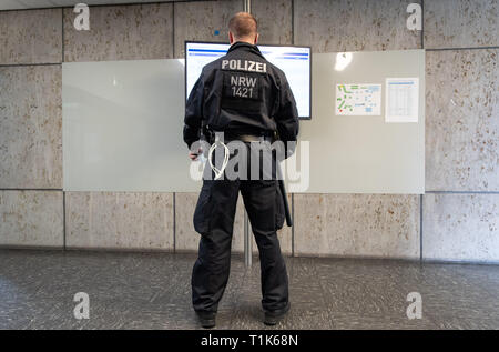 Bielefeld, Germany. 27th Mar, 2019. A policeman looks at a monitor in the district court. A trial against eight men on suspicion of a serious breach of the peace begins under great security precautions. The defendants, aged between 20 and 38, are to belong to an extended family. After an argument, one of the men was expelled from a discotheque. The 27-year-old is said to have called his brother and other relatives to it. The argument escalated. Credit: Friso Gentsch/dpa/Alamy Live News
