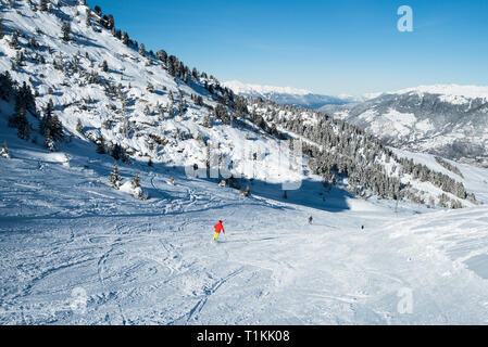 Panoramic landscape valley view with skiers going down a ski slope piste in winter alpine mountain resort Stock Photo