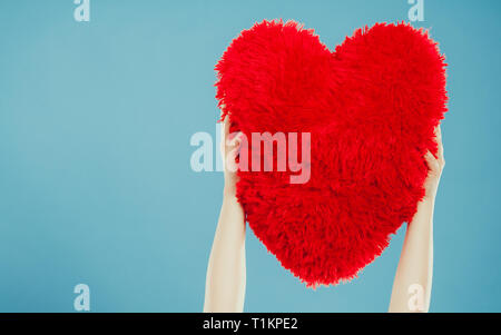 Red heart shape pillow in human hands in studio on blue. Valentines day love. Stock Photo