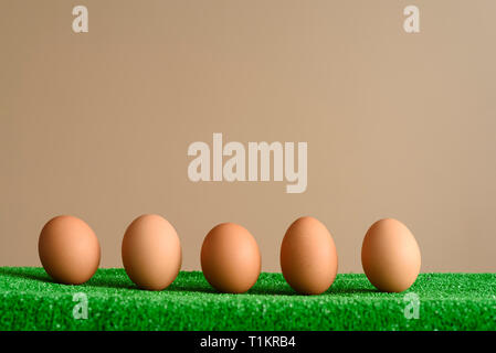Eggs in a line lying on a green surface as a bottom frane, with a brown background. Easter concept. Stock Photo