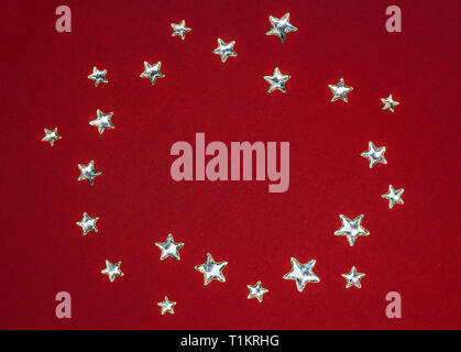Beautiful shining silver stars with embossed transparent top arranged in circle on deep red background. Copy space. Stock Photo