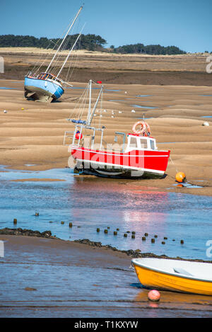 Colourful boats marooned on sandbanks at low tide on East Fleet river estuary at Wells next the sea, North Norfolk coast, East Anglia, England, UK. Stock Photo