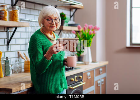 Aged woman looking at picture frame and enjoying morning coffee Stock Photo