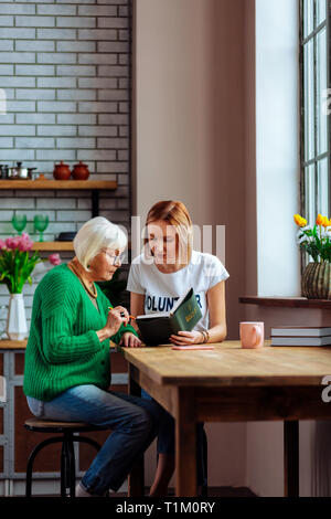 Young-adult woman reading Bible book with silver-haired religious retired dame Stock Photo