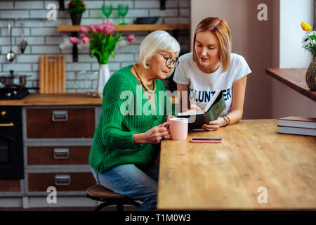 Pensioner listening to young lady reading Bible sitting at table Stock Photo