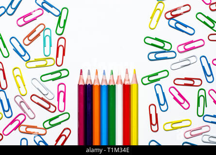 Many multi-colored stationery clips for documents and multi-colored pencils lie on a white background. Close-up Stock Photo