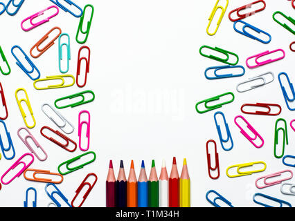 Many multi-colored stationery clips for documents and multi-colored pencils lie on a white background. Close-up Stock Photo