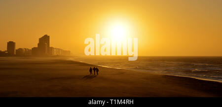 Panorama of a sunset along the North Sea beach of Ostend with the silhouette of three people walking during a sand storm, West Flanders, Belgium. Stock Photo