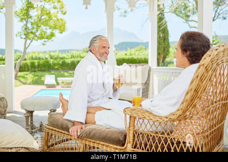 Mature couple in bathrobes relaxing, drinking mimosas in resort gazebo Stock Photo