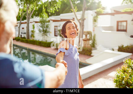 Happy, carefree mature couple holding hands at sunny resort poolside Stock Photo