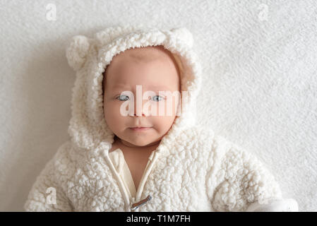 Beautiful baby girl in a warm white suit lying on a bed. Stock Photo