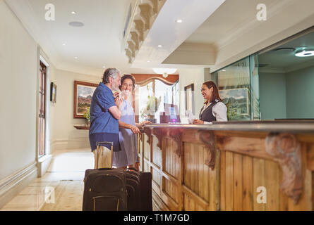 Mature couple with suitcases checking in at hotel reception Stock Photo