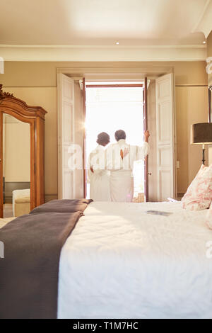 Affectionate couple in spa bathrobes standing at hotel balcony doorway Stock Photo