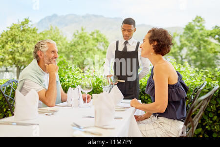 Wine steward pouring wine for mature couple dining at patio table Stock Photo