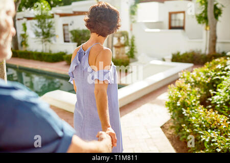 Couple holding hands, walking at sunny poolside